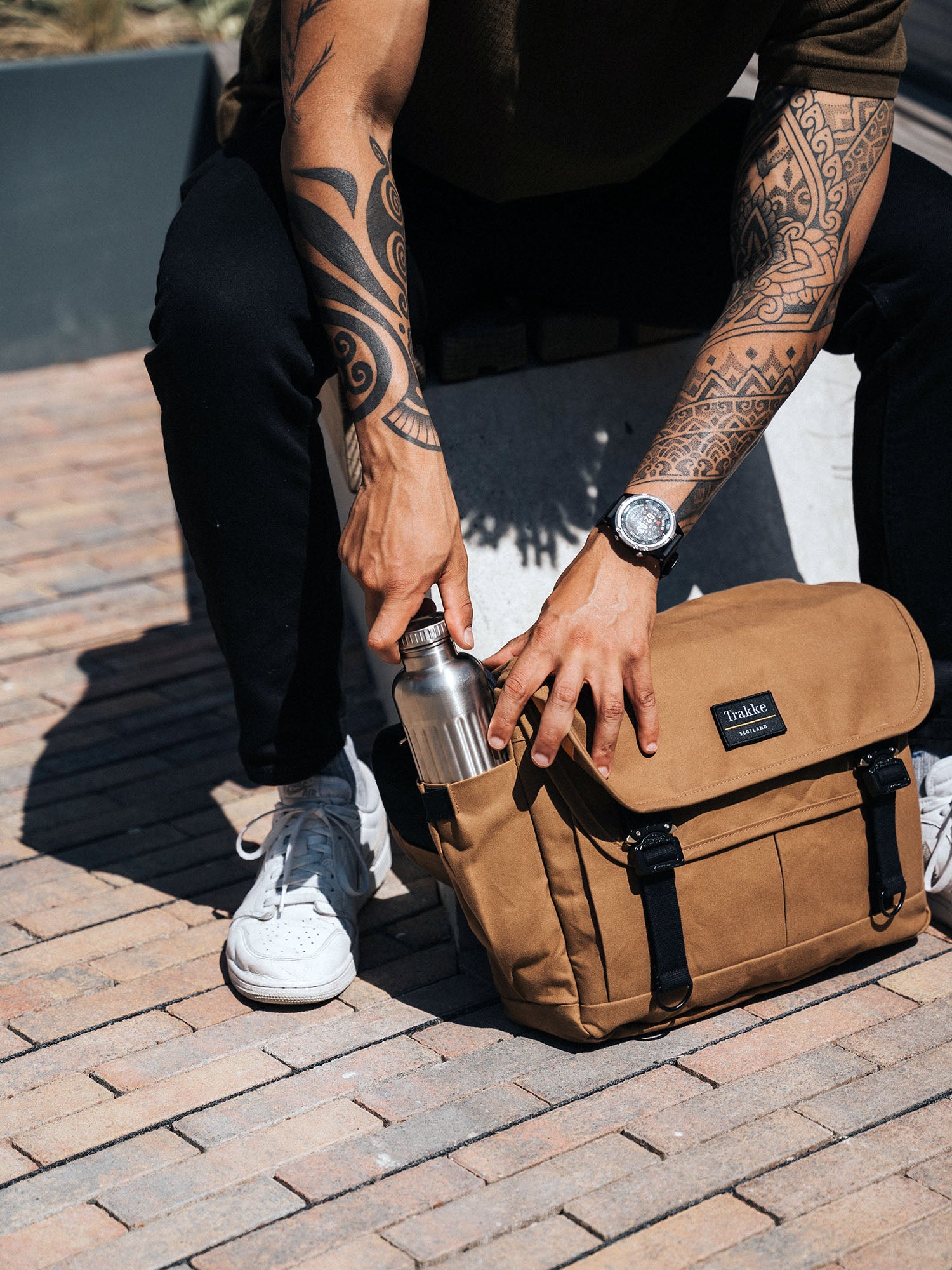 a person with tattoos on their arm putting a bottle into a bag