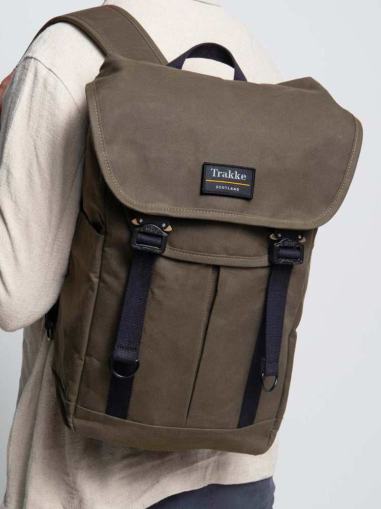 A male model is wearing the Trakke Bannoch Backpack in the Olive colourway. This version has the AustriAlpin COBRA clips on the backpack.