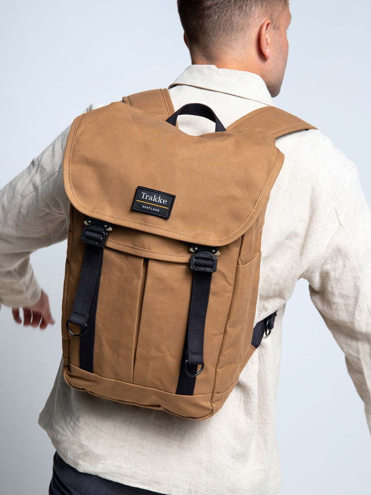 A man is wearing the Trakke Bannoch Backpack with COBRA Clips. The backpack is the Whisky colour. The Man is facing away from the camera with the focus on the backpack and he is swinging his arms at an angle.