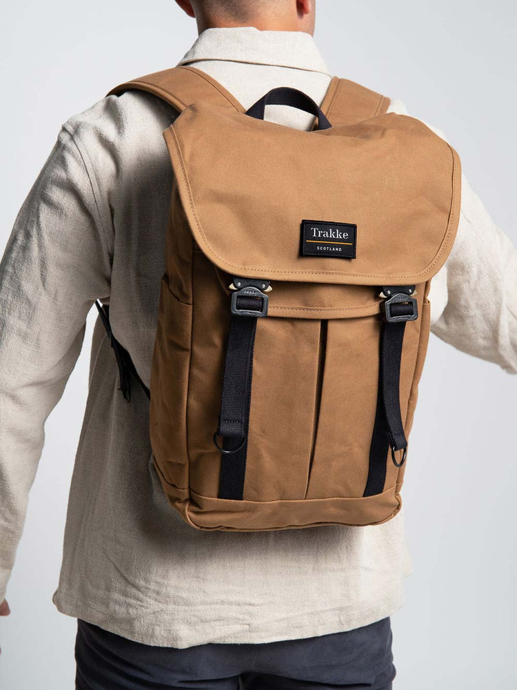 A man is wearing the Trakke Bannoch Backpack with COBRA Clips. The backpack is the Whisky colour. The Man is facing away from the camera with the focus on the backpack and he is swinging his arms