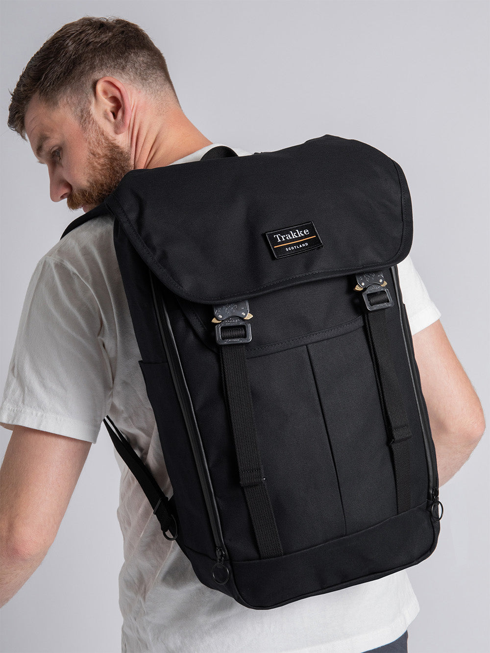The Bannoch Pro Backpack from Trakke - a man is wearing the bannoch pro backpack on his back, the colour of the backpack is black. The image shows the full length of the backpack and a few features such as two COBRA buckles, the trakke velcro patch and external zips