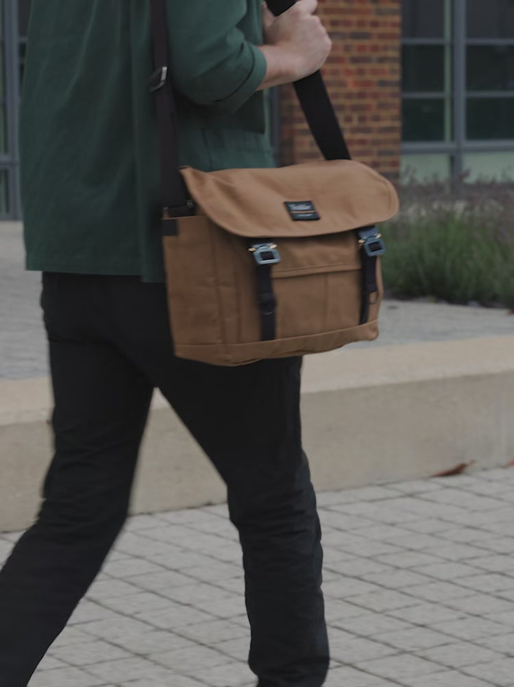 a man walking and then unbuckling a whisky coloured version of the Bairn Pro Messenger