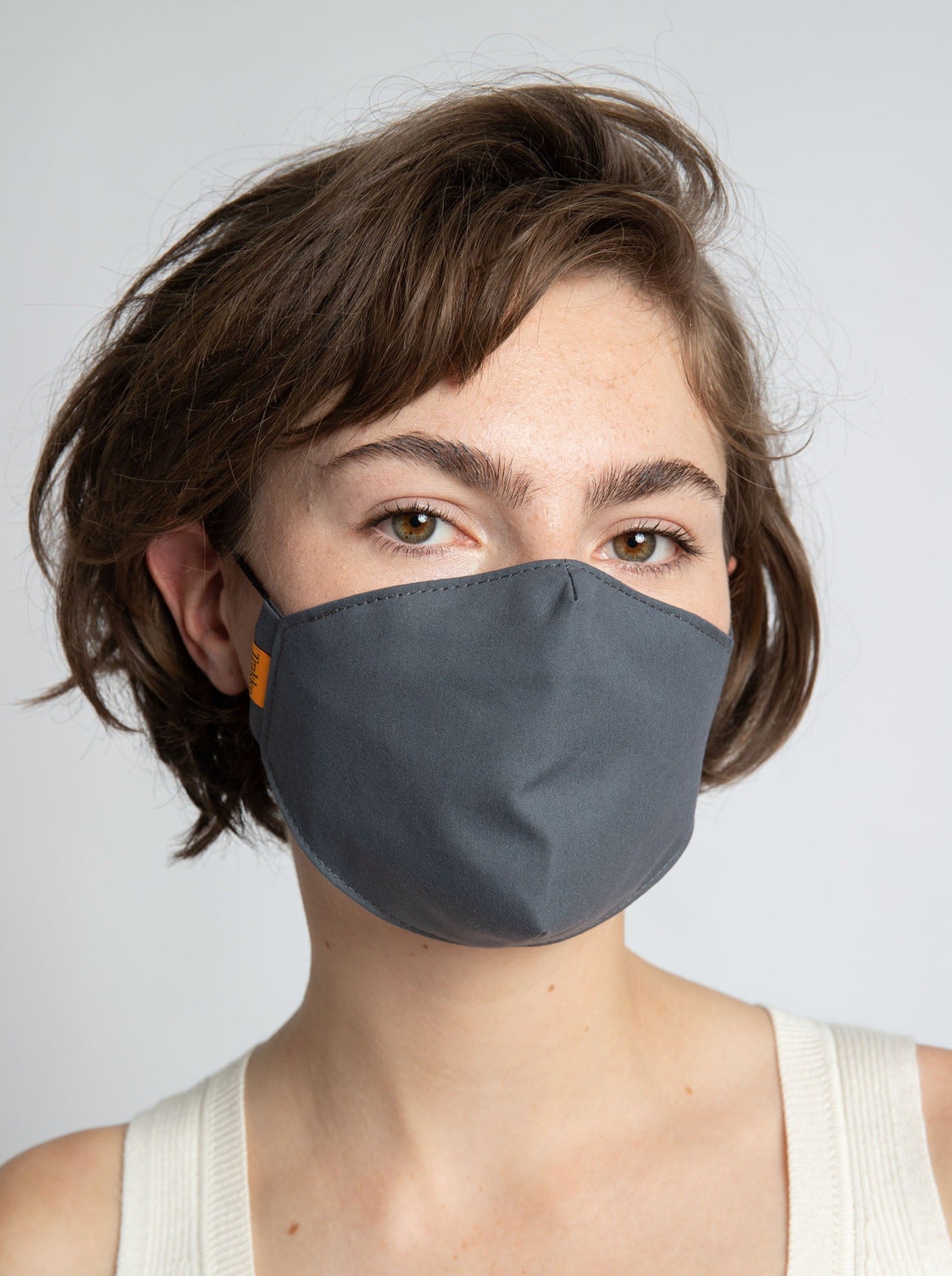 Picture of woman wearing a Trakke Face Mask in Grey - made of treated canvas with black elastic ear loops. Designed to fit disposable N95 air filters