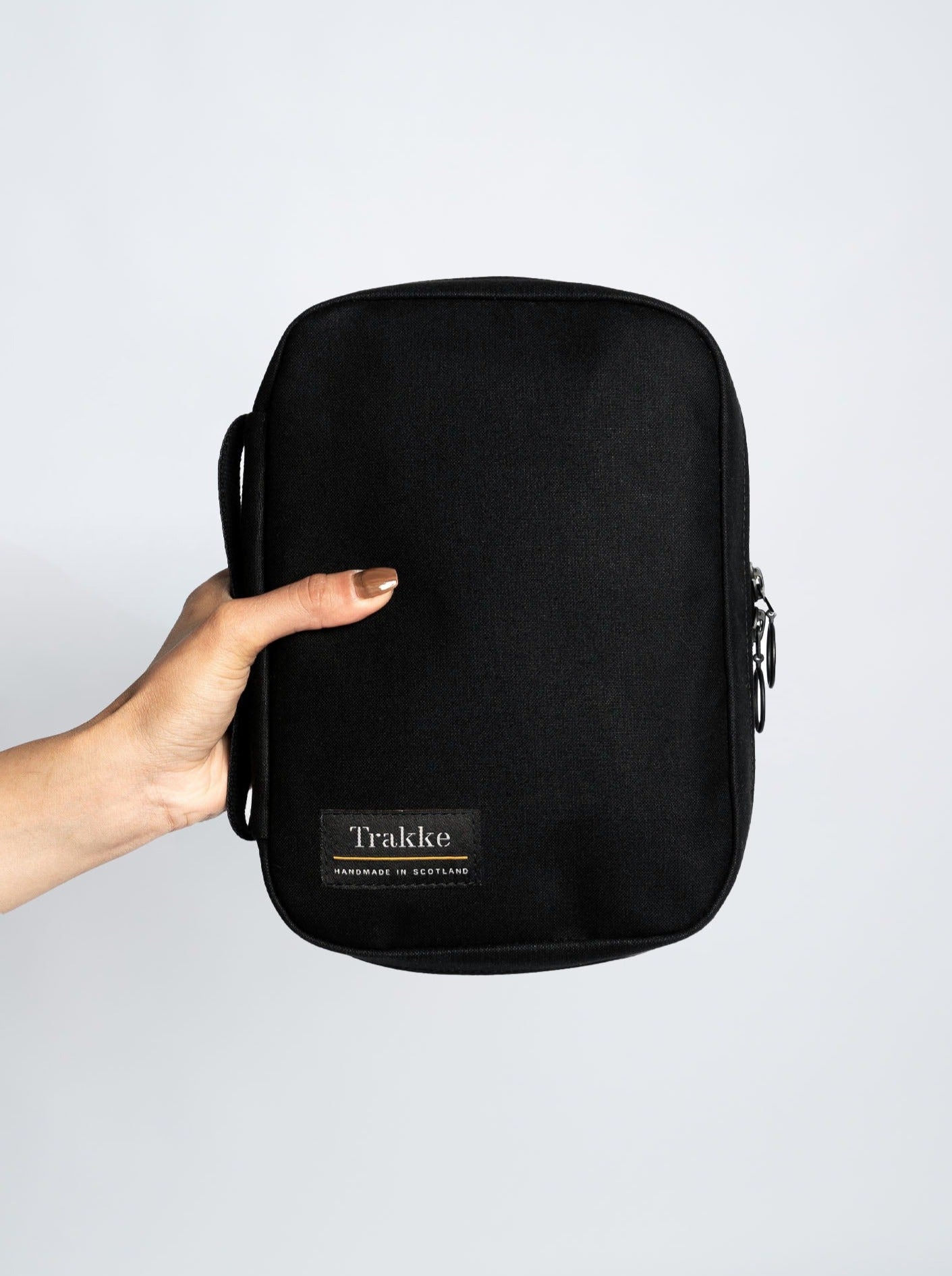 Picture of a person holding the Trakke Laggan Pro in Black. Made of dry-finish waxed canvas with black cotton webbing grab handle and Trakke logo in left corner.